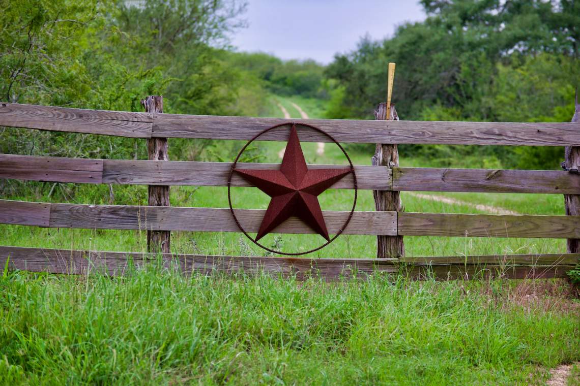 Texas rustic star on countryside side wooden fence, with road to the house slowly dissolving in the background.