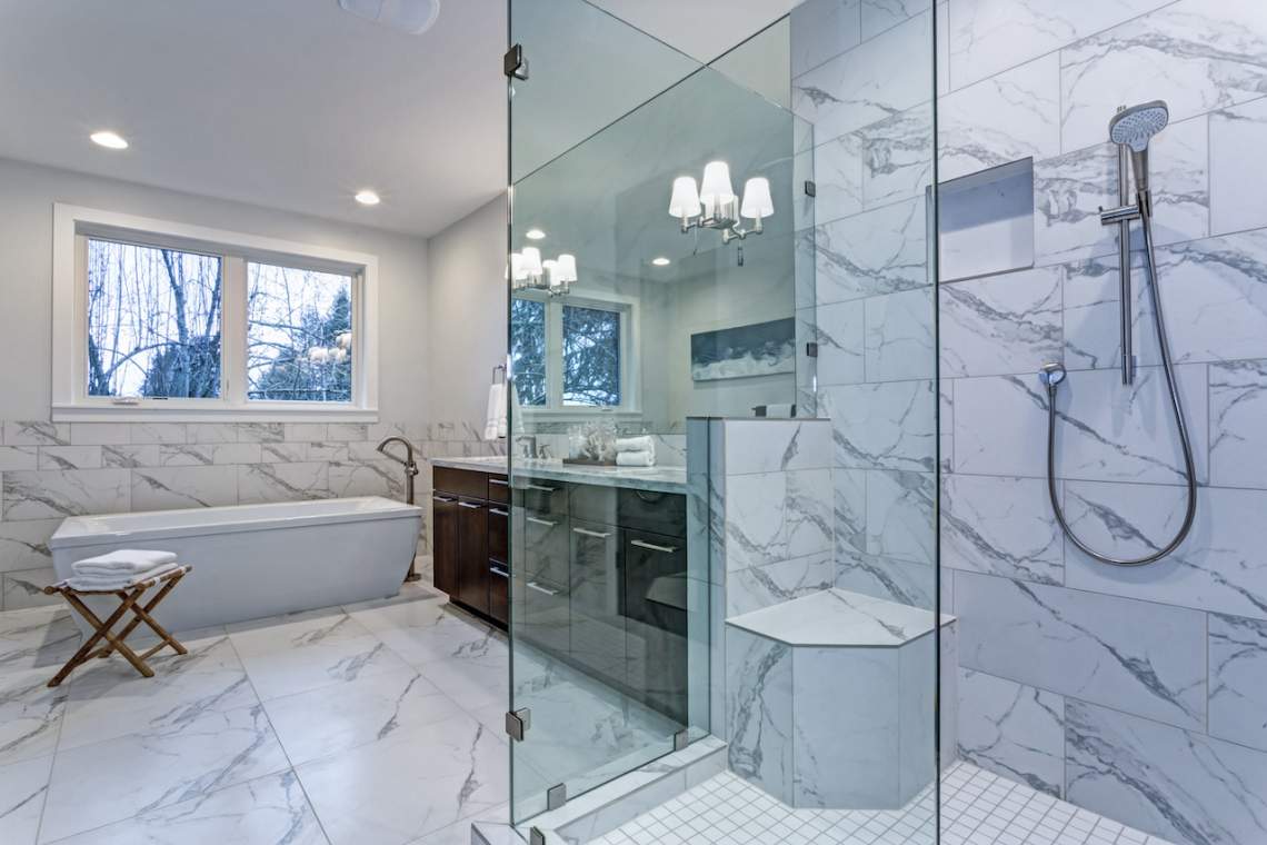 Incredible master bathroom with Carrara marble tile surround, modern glass walk in shower, espresso dual vanity cabinet and a freestanding bathtub.